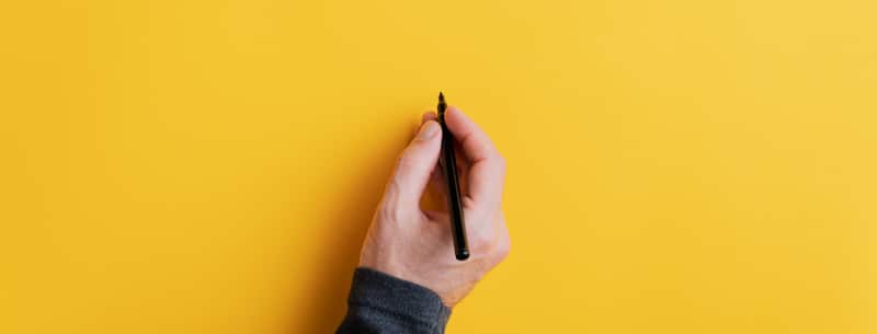 hand holds pen to write on yellow background