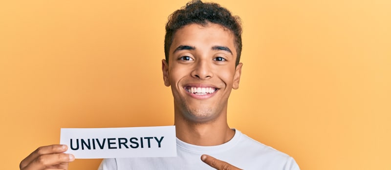 smiling young man points at university sign