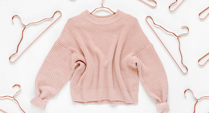 baby pink sweater surrounded by hangers